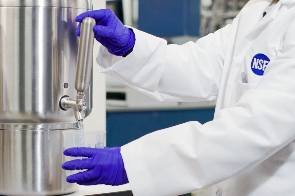 Person in white lab coat and purple gloves operating a metallic device.