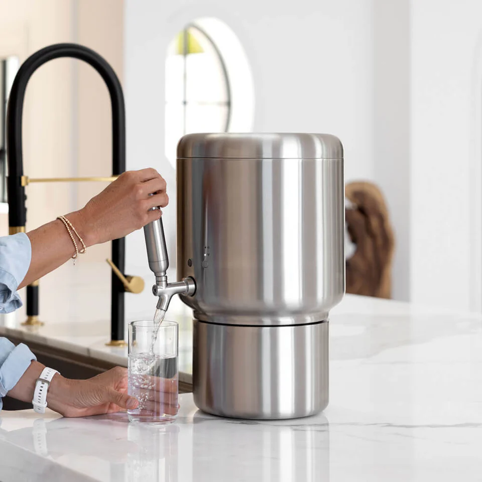 Stainless steel water filter being used to fill a glass with water.